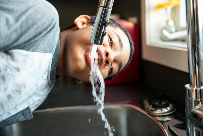 Junge trinkt aus laufendem Trinkwasserhahn Wasser 